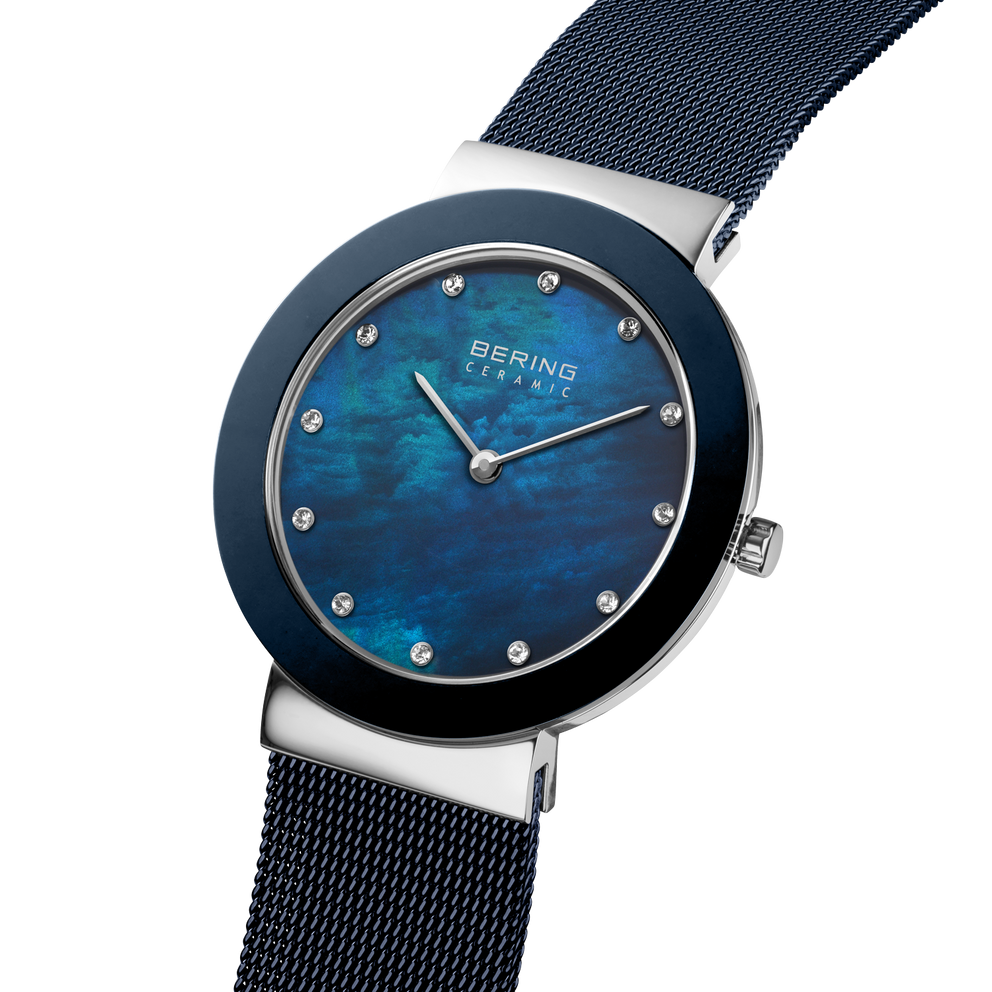 Angled close-up of the mottled blue dial and silver-tone with blue bezel case beside the blue mesh strap.
