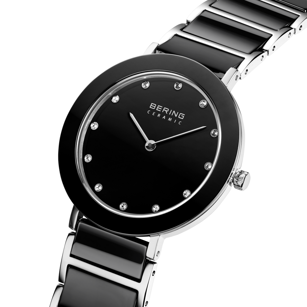 Angled close-up of the black dial with bright dot markers and silver-tone with black bezel case beside the black-centered silver-tone link bracelet.