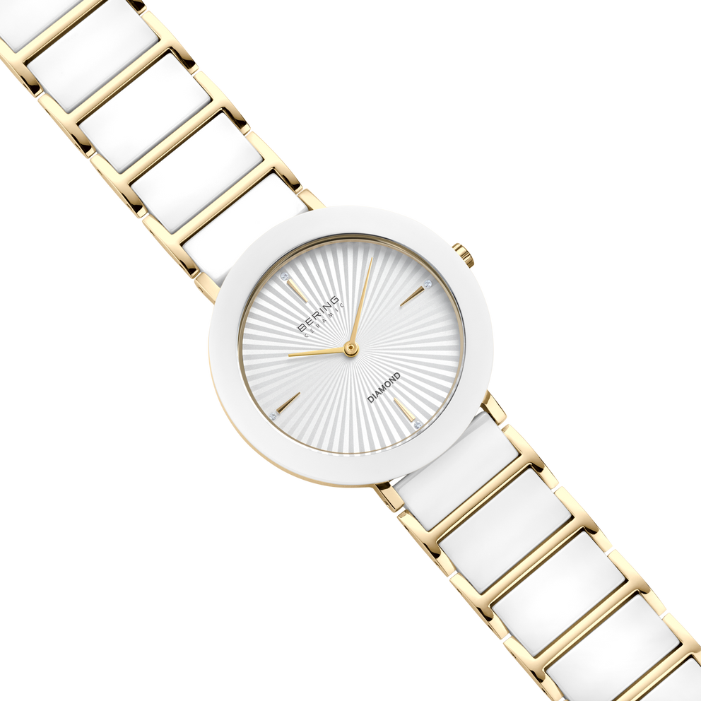 Vista diagonal desde arriba: esfera blanca con líneas radiales, caja dorada con bisel blanco y pulsera dorada de eslabones con centros blancos.
