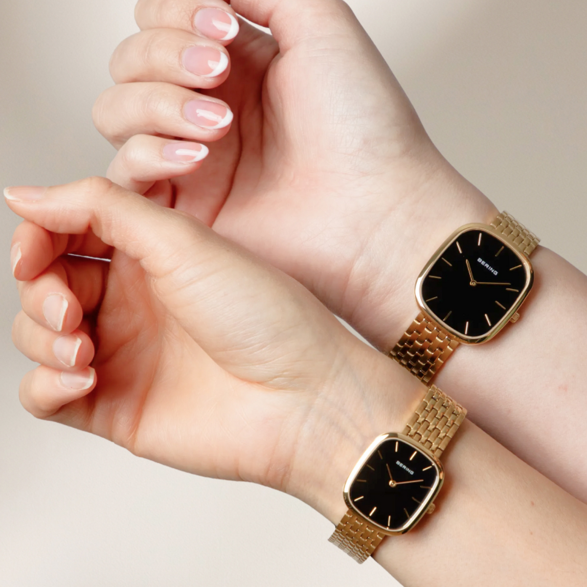 Two wrists wearing different sizes of gold-tone rectangular watches with black dials and link bracelets.