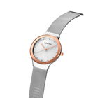 Angled close-up of the pale dial with bright dot markers and oval rose-tone case beside the silver-tone mesh strap.