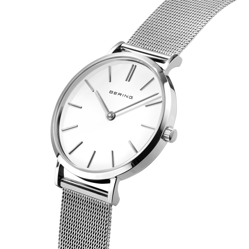 Angled close-up of the white dial and silver-tone case beside the silver-tone mesh strap.