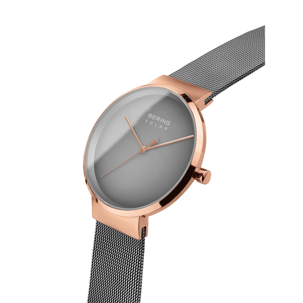 Angled close-up of the grey dial and rose-tone case beside the grey mesh strap.