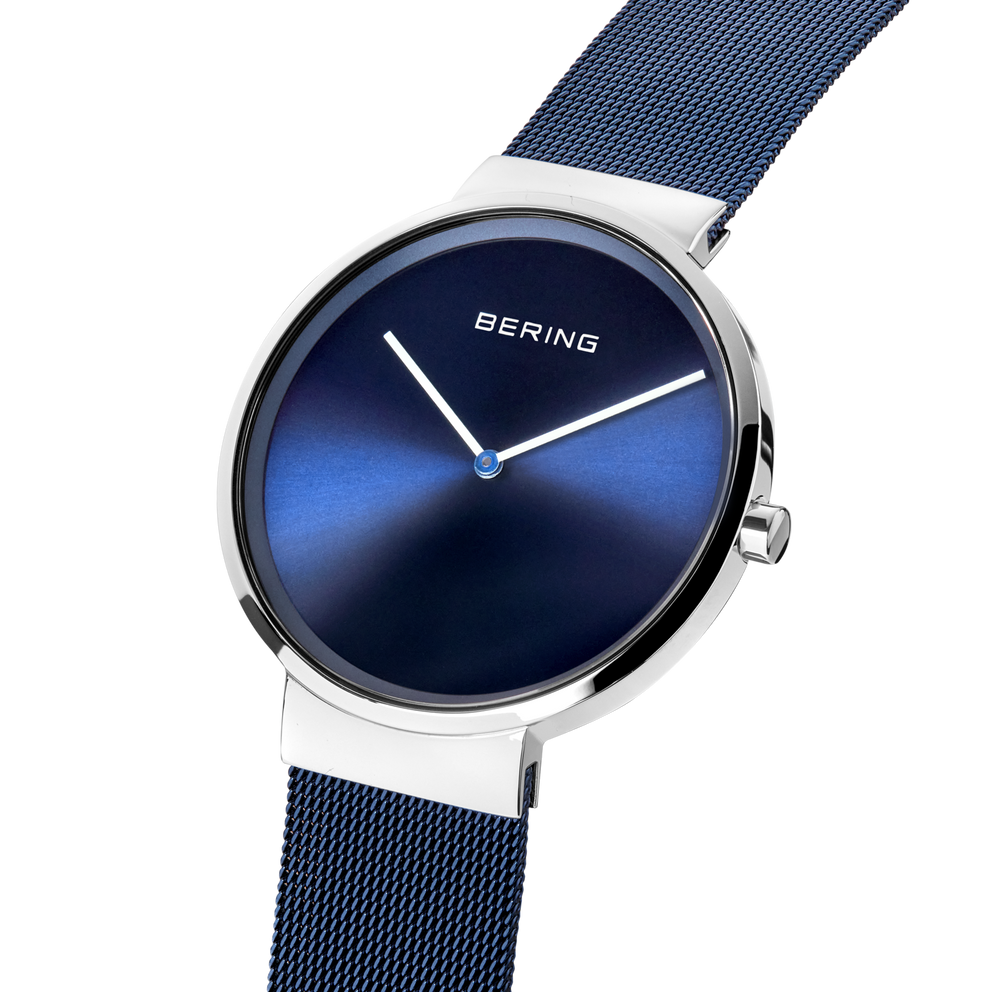 Angled close-up of the blue dial and silver-tone case beside the blue mesh strap.
