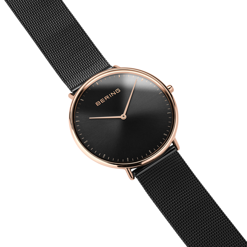 Diagonal overhead view of the black dial, rose-tone case and black mesh strap.