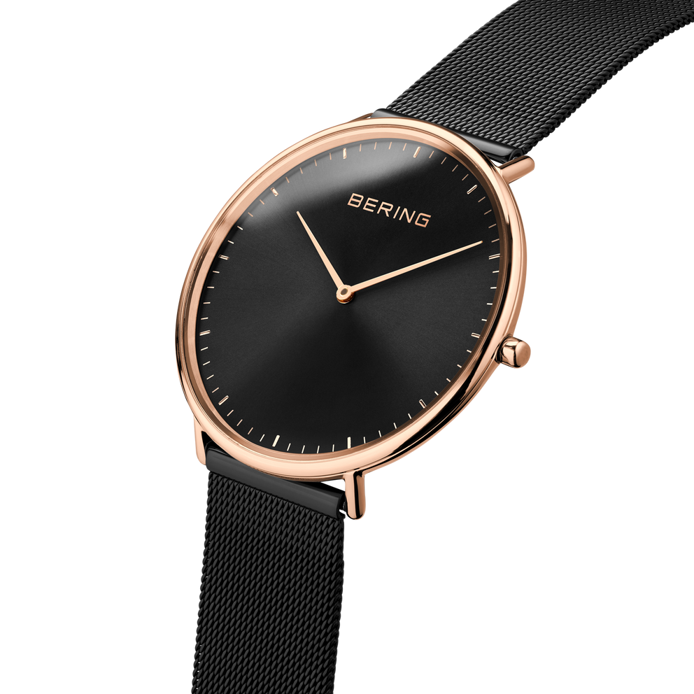 Angled close-up of the black dial and rose-tone case beside the black mesh strap.