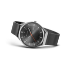 Angled watch view: grey dial with an orange hand and grey mesh strap extended.