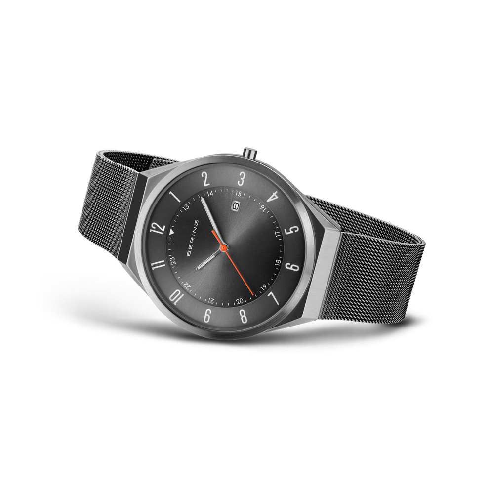 Angled watch view: grey dial with an orange hand and grey mesh strap extended.