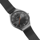 Diagonal overhead view of the grey dial with an orange hand, grey case and grey mesh strap.