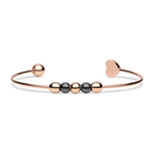 Brazalete abierto rosado con cuentas oscuras y un extremo liso de corazón, tumbado.